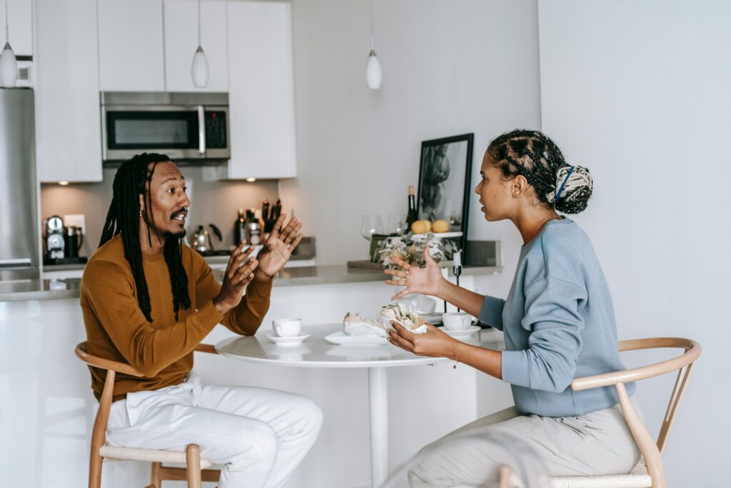 A couple seated at a kitchen table, actively engaged in conversation, symbolizing open communication and conflict resolution in relationships.