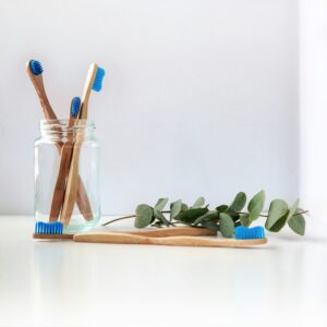 Wooden toothbrushes in a glass jar beside a eucalyptus branch, representing healthy self-care and stewardship of the body.