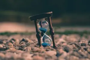 An hourglass with blue sand resting on pebbles, symbolizing the passage of time and the importance of biblical time management.